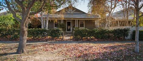 A two-story house with a front porch, surrounded by trees and a lawn covered with fallen leaves.