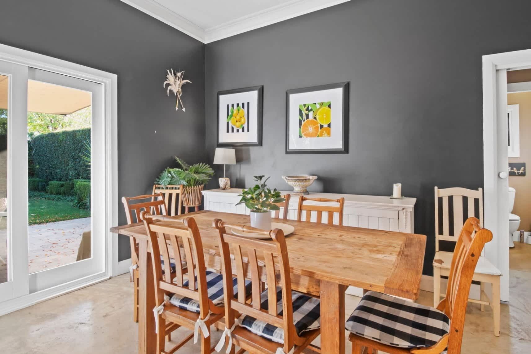 A dining area with a wooden table and chairs, a white radiator, and two framed pictures on the wall.