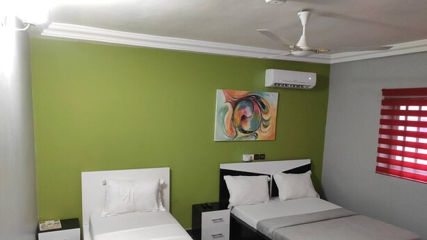 A bedroom with two beds, a ceiling fan, an air conditioning unit, and a window with blinds.