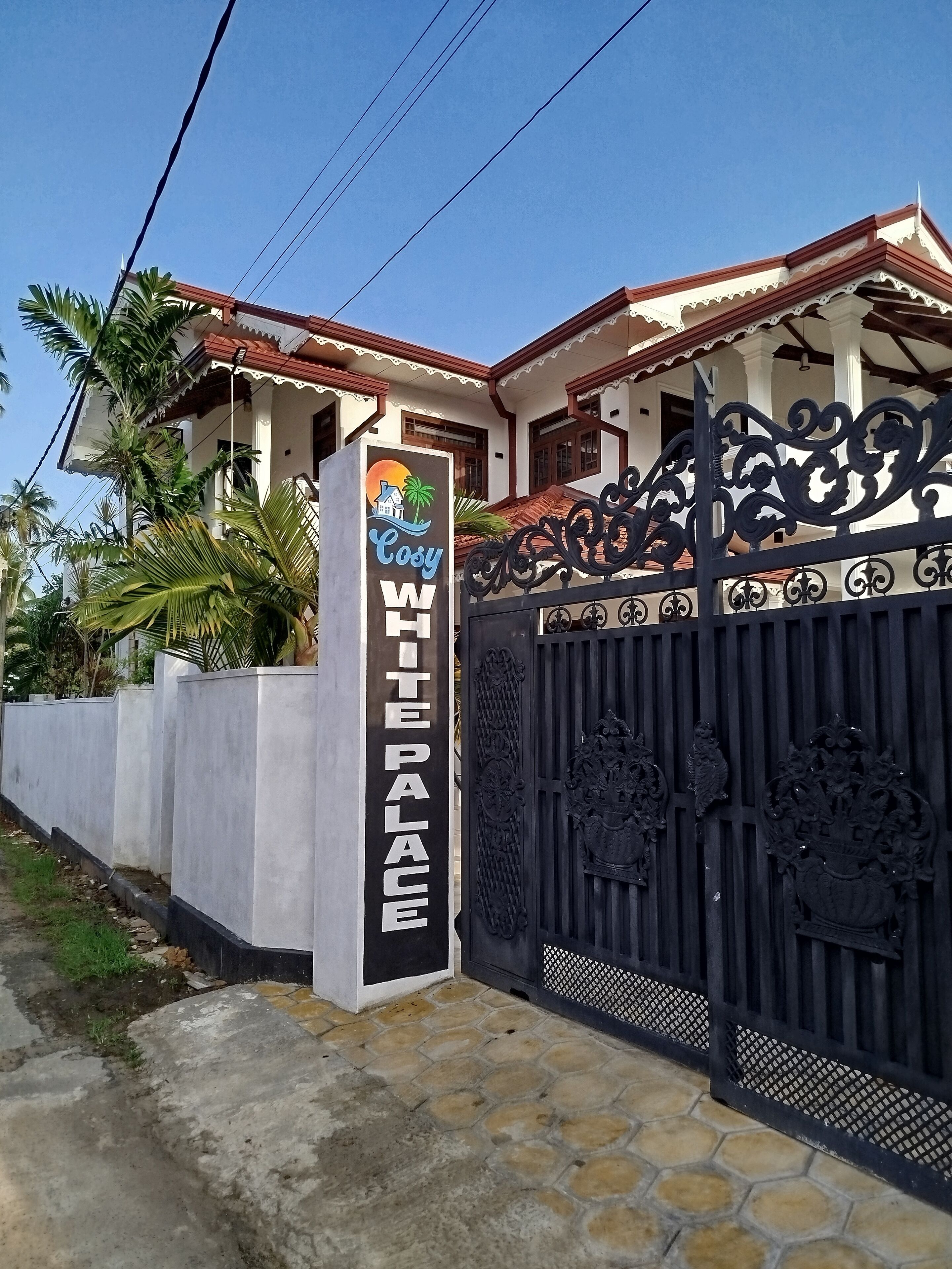 A gated entrance to a white building with a sign reading "Cozy White Palace."