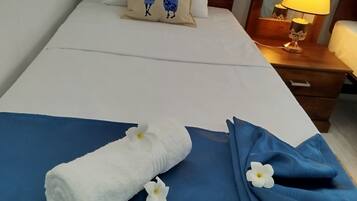 Una cama bien tendida con un edredón azul, una toalla blanca con flores y una almohada con un diseño cultural.