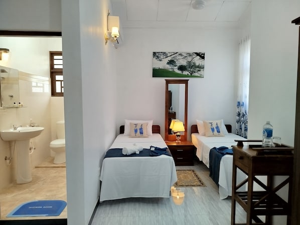 A hotel room with two beds, a bathroom, a painting, and a nightstand with a lamp. - Cosy White Palace (Negombo)