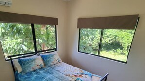 Une chambre à coucher avec un lit, un ventilateur de plafond et de grandes fenêtres donnant sur un paysage verdoyant.