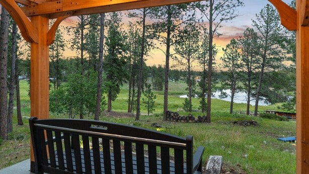 Eine Holzpergola mit Lichterketten, einer Bank und Blick auf einen Wald und See.