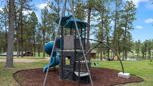 Ein Spielplatz mit Rutsche, Schaukel und Klettergerüst, umgeben von Bäumen.