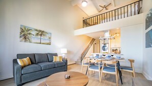 A modern living room with a grey sofa, a round wooden coffee table, and a dining area with a wooden table and chairs. - Top Floor, 360 deg Ocean View, Totally Remodeled, 2-bed 2 bath with split AC (Kihei)