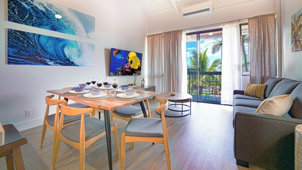 A modern living room with a dining area, featuring a large window with curtains, a sofa, and artwork on the walls. - Top Floor, 360 deg Ocean View, Totally Remodeled, 2-bed 2 bath with split AC (Kihei)