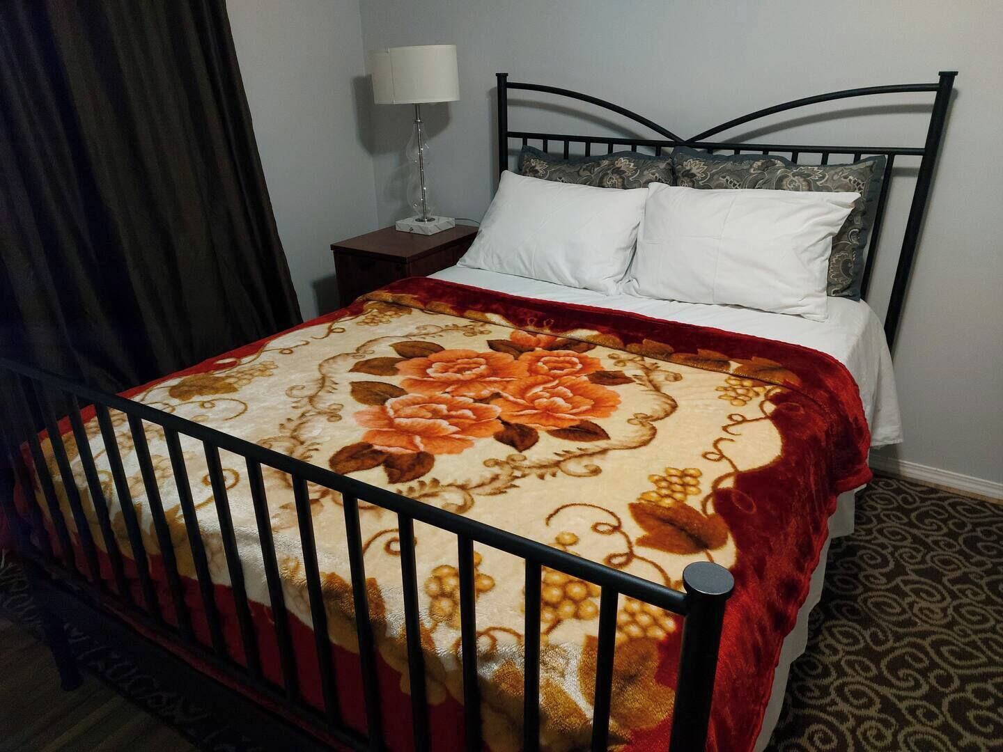 A neatly made bed with a floral bedspread, a black metal headboard, and a bedside table with a lamp.