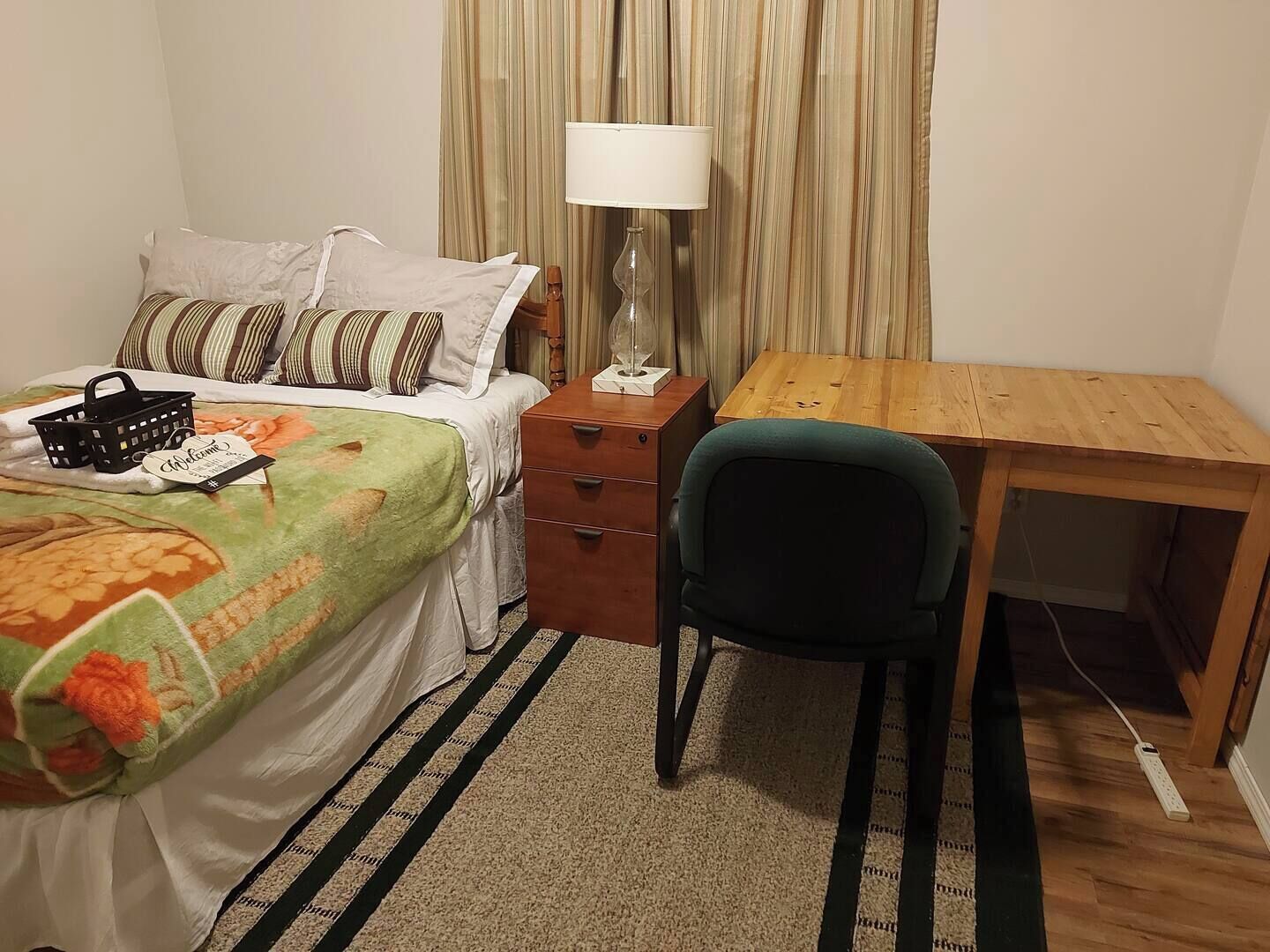 A hotel room with a bed, a desk, a chair, a lamp, and a curtain.