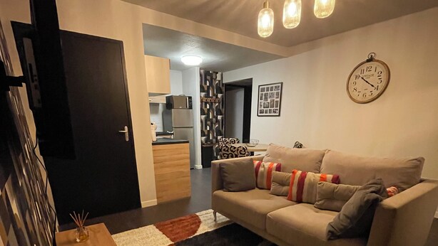A modern living room with a sofa, a coffee table, and a rug. There is a kitchen in the background with a refrigerator and a microwave. - Apartment t2 floor at the edge of the lot (Espalion)