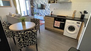A compact living space with a dining area, a kitchen with a washing machine, and a TV mounted on the wall. - Apartment t2 floor at the edge of the lot (Espalion)