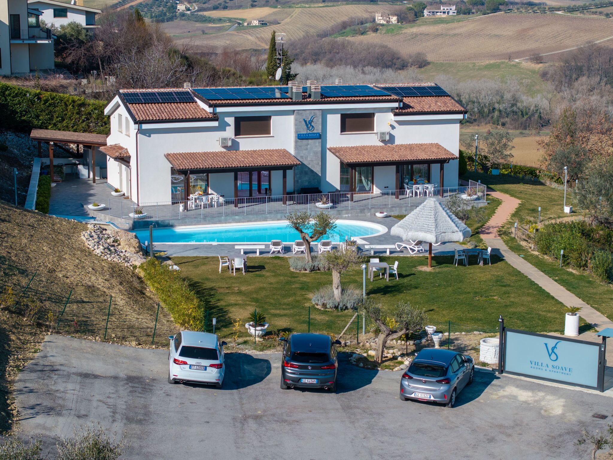 Una villa moderna con piscina, area relax all'aperto e auto parcheggiate.
