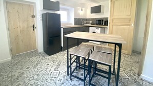 Ett kompakt kök med kylskåp, mikrovågsugn, tvättmaskin och ett träbord med stolar.