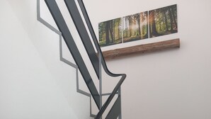 A wooden staircase with a metal handrail and a wall-mounted picture of a forest. - Ankommen, Entspannen & Genießen - Gemütliches Apartment mit Traumhaftem Ausblick (Lalling)