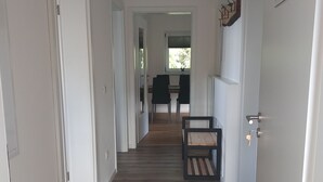 A hallway with wooden flooring, white walls, and a door on the right. There is a small table with chairs in the distance. - Ankommen, Entspannen & Genießen - Gemütliches Apartment mit Traumhaftem Ausblick (Lalling)
