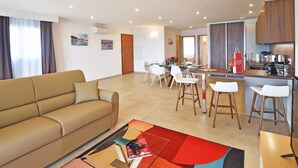 Uma sala de estar moderna com um sofá, uma mesa de centro, uma área de jantar com cadeiras e um balcão de cozinha.
