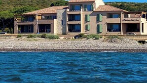 Um edifício costeiro com fachada de pedra, várias varandas e vista para o mar.