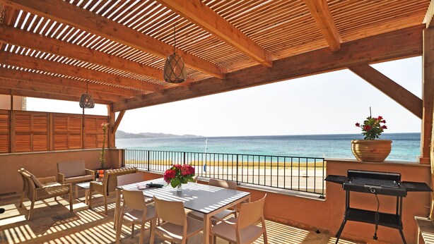 Um deck de madeira com mesa, cadeiras, churrasqueira e vista para o mar.