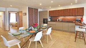 Cozinha moderna com armários de madeira, mesa de jantar de vidro e cadeiras brancas.