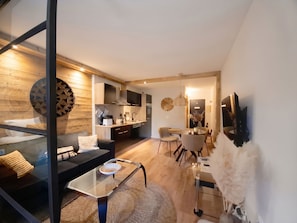 A modern living space with a glass coffee table, a sofa, a dining area with chairs, and a kitchen with appliances.