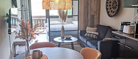 A modern hotel room with a dining area, a sofa, a TV, and a large window.