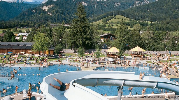Ein Schwimmbeckenbereich mit mehreren Wasserrutschen, umgeben von einer gebirgigen Landschaft.