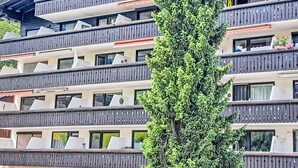 Ein mehrstöckiges Gebäude mit Balkonen, großen Fenstern und einem Baum davor.