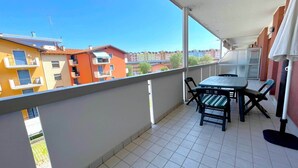 A balcony with a table and chairs, overlooking a residential area with colorful buildings. - Apartment in Caorle near Sea Beach & Pool (Caorle (VE))