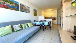 A modern living room with a sofa, dining table, chairs, and a TV. - Apartment in Caorle near Sea Beach & Pool (Caorle (VE))