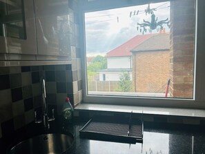 Enjoy a view of the surrounding neighborhood from this kitchen, featuring a stainless steel sink and a tiled backsplash.
