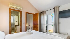 Une chambre d’hôtel avec un grand lit, un téléviseur fixé au mur et une salle de bain visible à travers une porte ouverte.