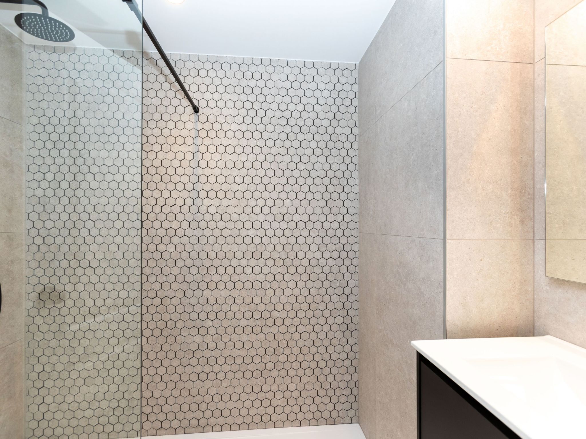 Une salle de bain moderne avec des carreaux à motifs hexagonaux, un espace douche et un plan de toilette blanc.