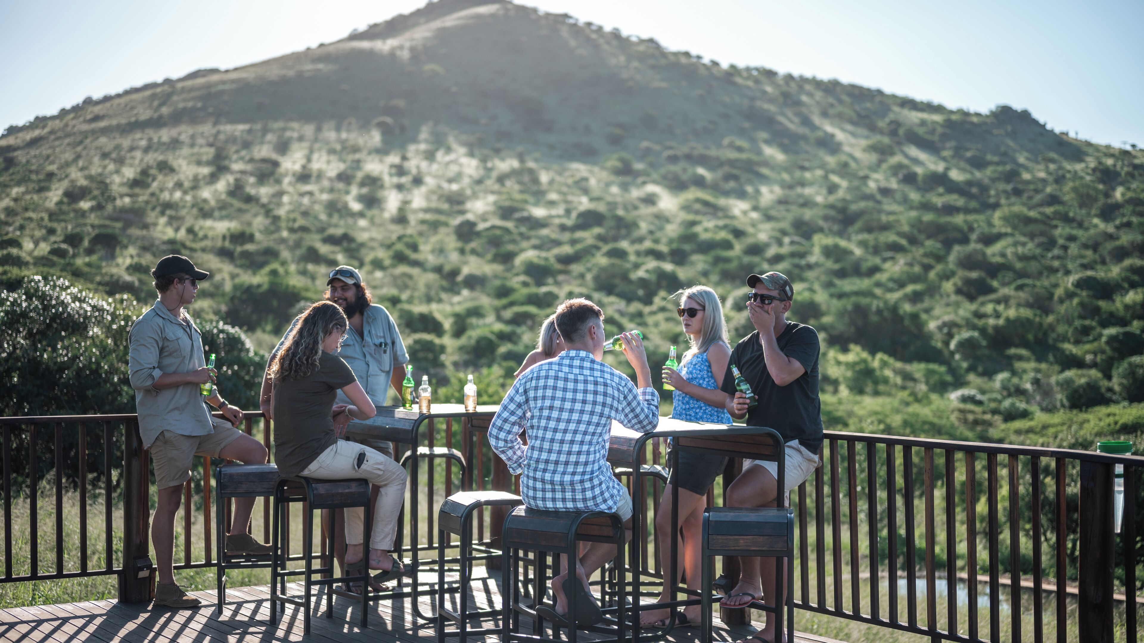 A group of people sitting at an outdoor table with a view of a hill in the background.