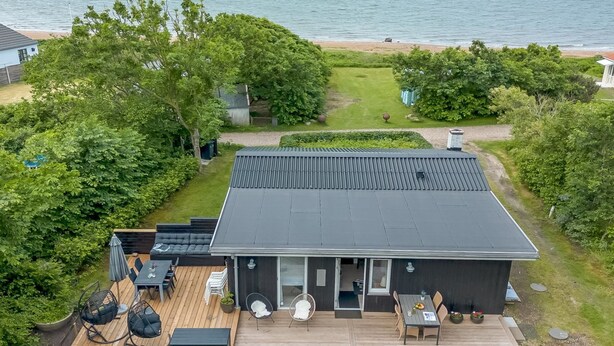 Une maison moderne avec un toit plat, une terrasse en bois et un espace patio aménagé avec du mobilier d’extérieur.