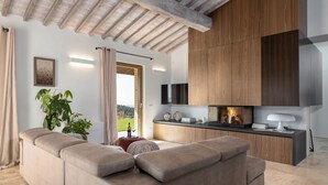 A modern living room with a sectional sofa, a fireplace, and a kitchen area with wooden cabinets. - Private Villa with hot tub, private pool, A/C, WIFI, patio, pets allowed, close to San Gimignano (Volterra)