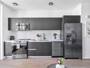 A modern kitchen with grey cabinetry, stainless steel appliances, and white subway tiles.