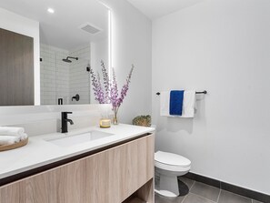 A modern bathroom with a white sink, a mirror, a toilet, and a towel rack.