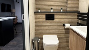 A modern bathroom with a wooden wall, a toilet, a sink, and a small trash bin.
