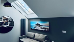 Un salon moderne doté d’une lucarne, d’un grand miroir rond, d’un canapé gris et d’un tableau représentant un paysage.