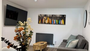 A modern living room with a grey sofa, a wooden coffee table, and a vibrant painting of surfboards on the wall.