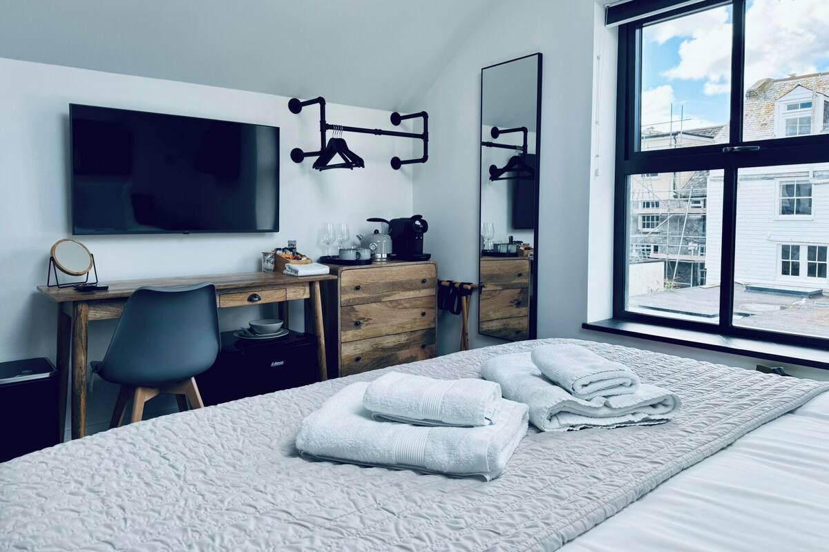 Una habitación de hotel moderna con una cama grande, un escritorio con silla, un televisor de pantalla plana y un amplio ventanal con vistas a la ciudad.