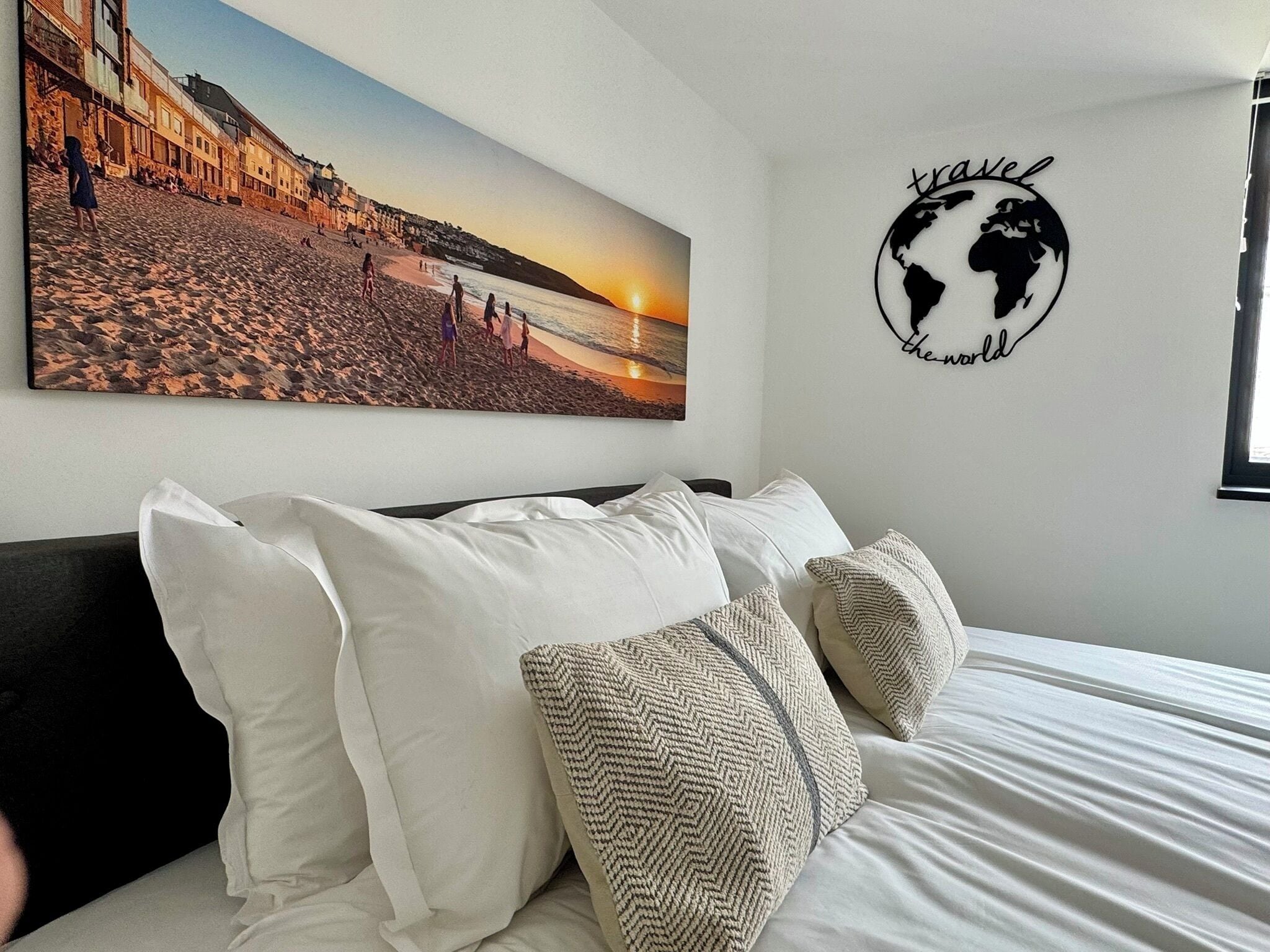 A bedroom with a bed, white pillows, and a wall art of a beach scene.