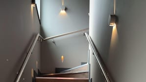 Un escalier moderne avec des marches en bois et des rampes en métal, éclairé par des appliques murales.