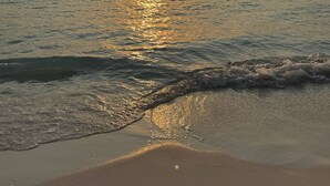 A beach with the sun setting over the ocean, waves gently lapping at the shore.
