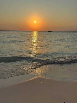 Una platja amb el sol ponent-se sobre l'oceà, ones que brollen suaument a la riba.