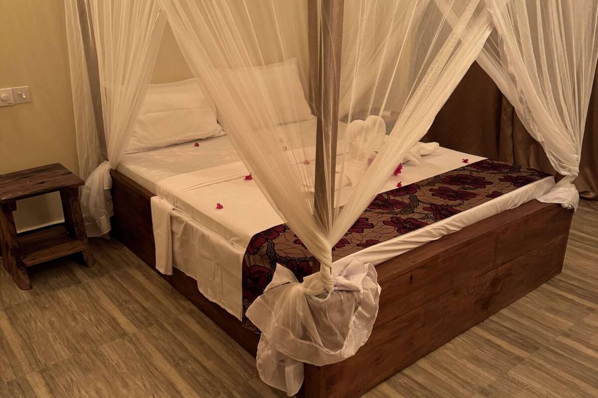 A wooden four-poster bed with a white canopy, a small wooden nightstand, and a floral-patterned bedspread.