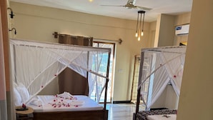 Habitación de hotel con dos camas, cada una con dosel, un ventilador de techo y una tetera sobre una mesa.