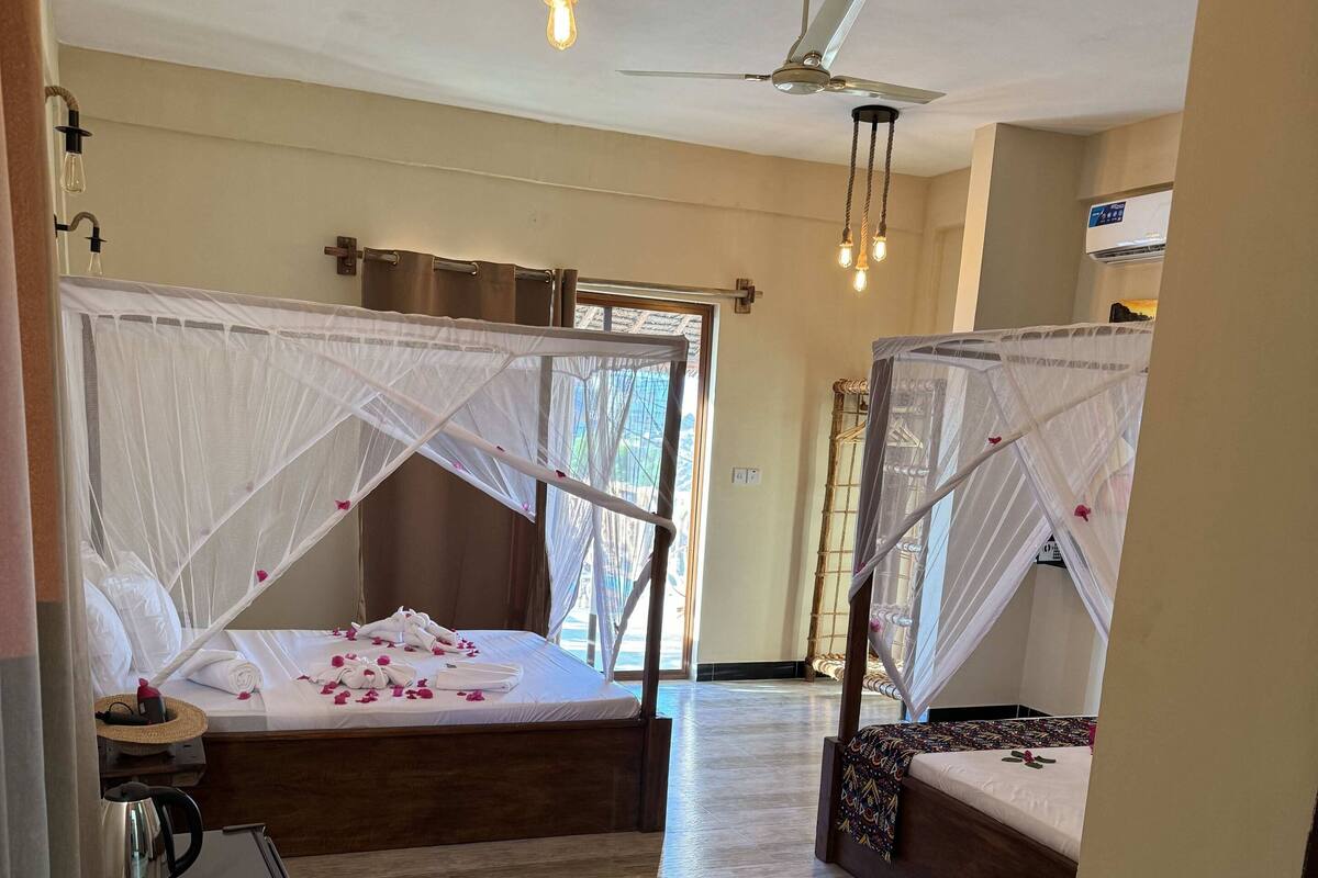 A hotel room with two beds, each with a canopy, a ceiling fan, and a kettle on a table.
