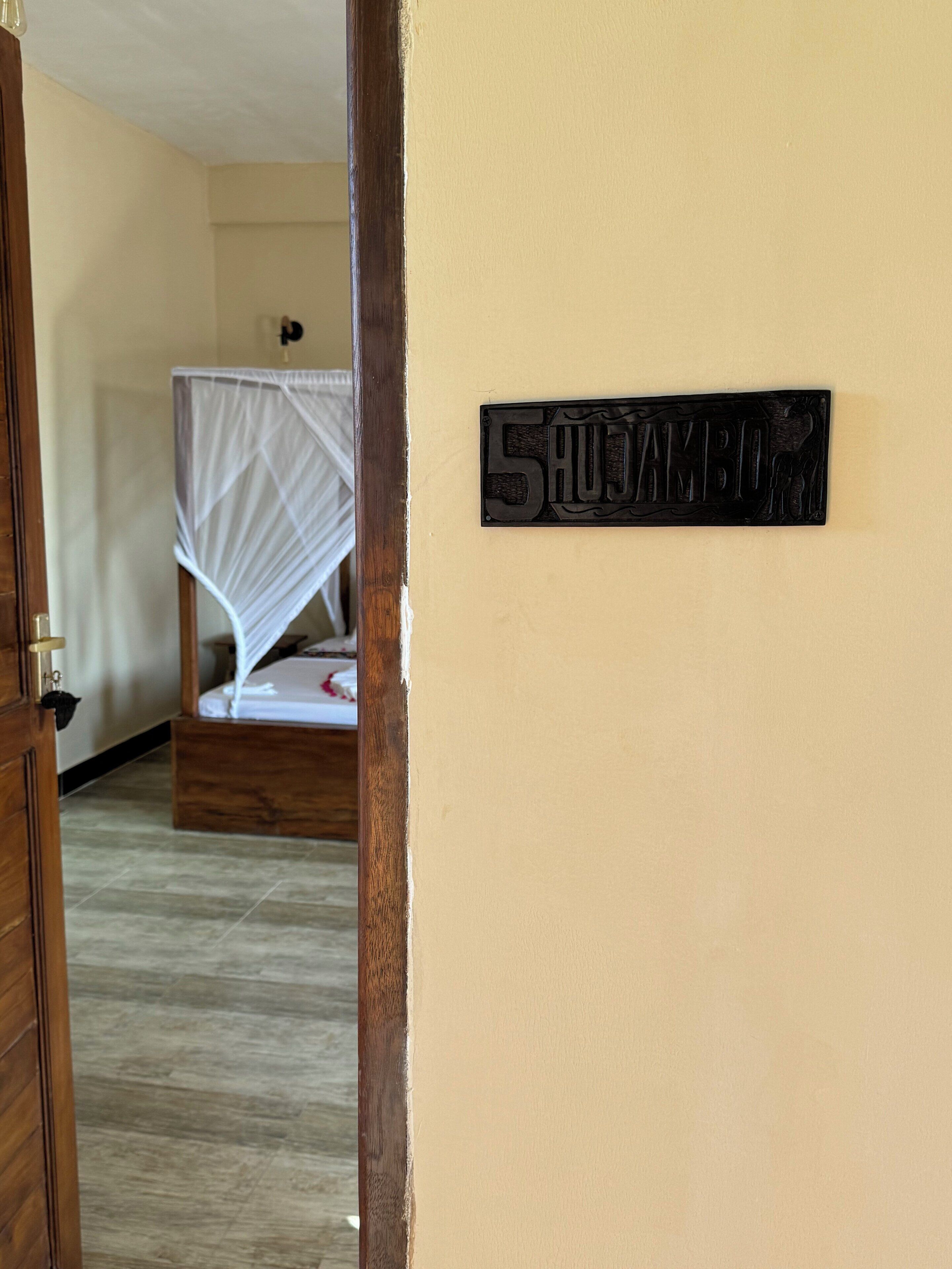 Quarto com uma cama, moldura de porta de madeira e placa na parede com o número 5.