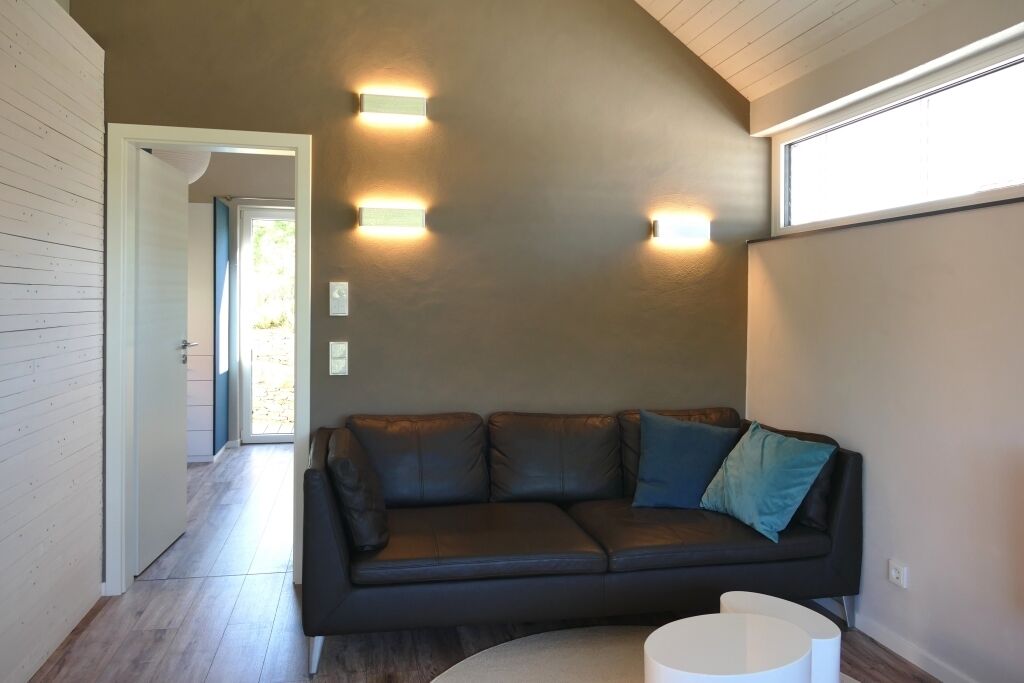Un salon moderne avec un canapé en cuir foncé, une table basse blanche et des luminaires fixés au mur.